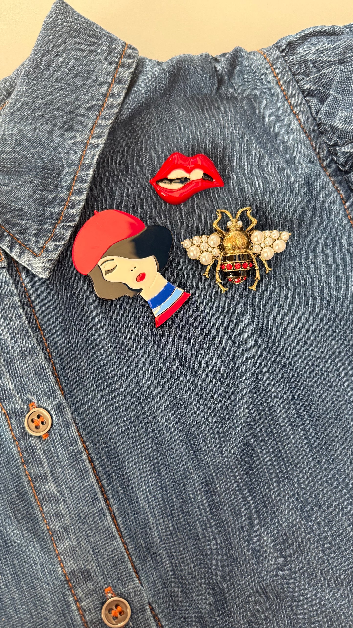 Three-piece Emily in Paris brooch set on denim shirt showing French girl, lips, and bee
