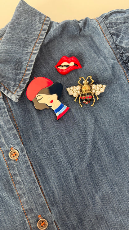 Three-piece Emily in Paris brooch set on denim shirt showing French girl, lips, and bee