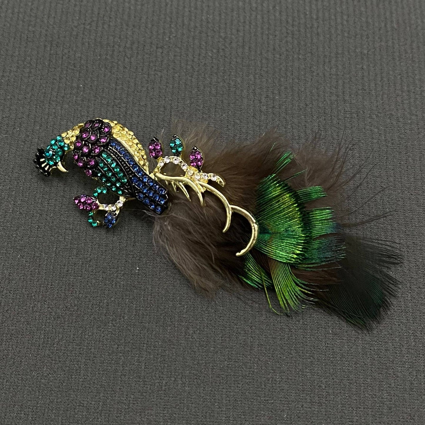 Decorative peacock brooch with feathers and gemstones on a gray background