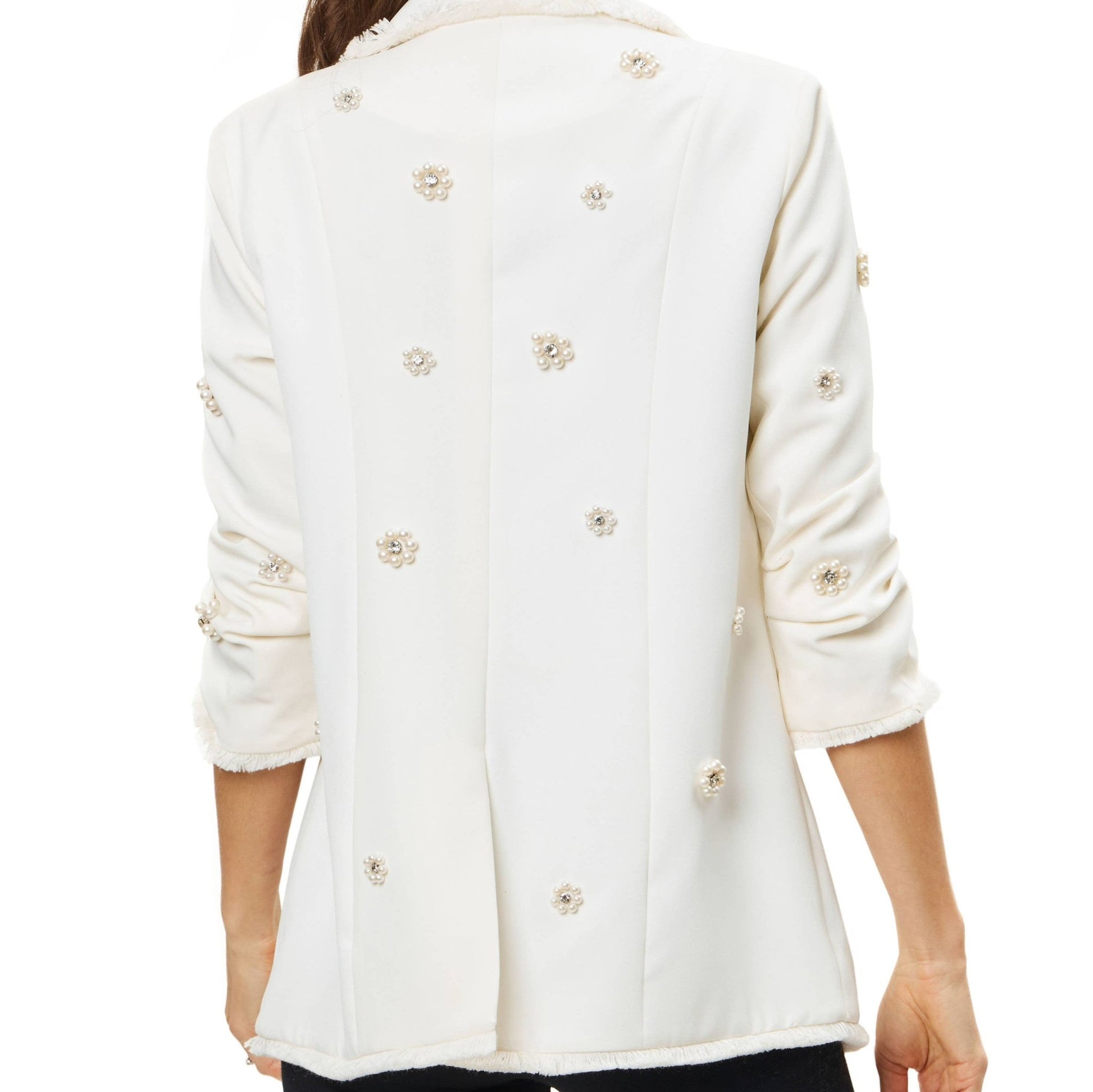 Back view of woman wearing a white blazer with pearl and rhinestone embellishment in front of a white background