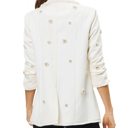 Back view of woman wearing a white blazer with pearl and rhinestone embellishment in front of a white background