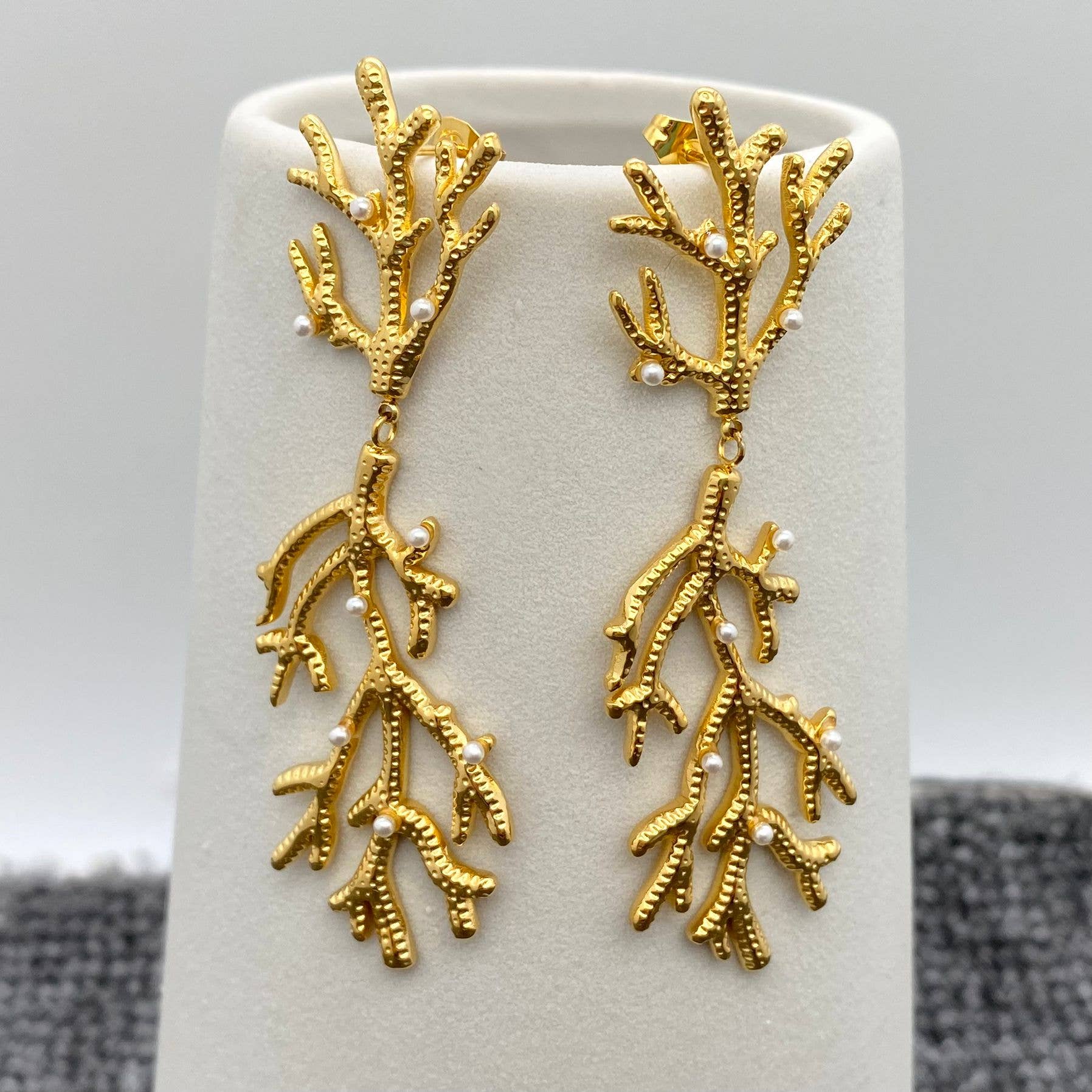 a pair of pearl encrusted gold coral shaped earrings on white stand