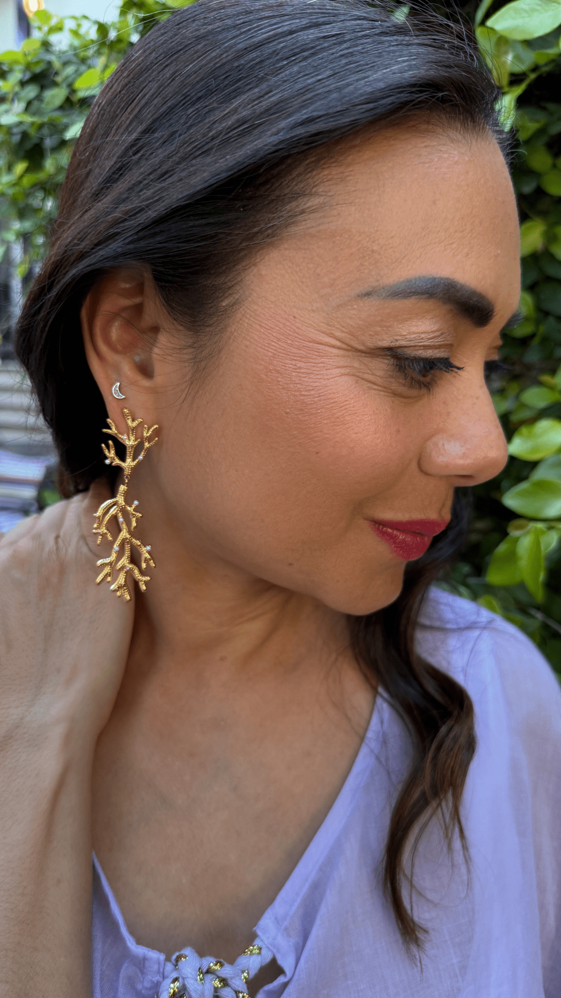 Woman wearing gold coral shaped earrings with a green leafy background