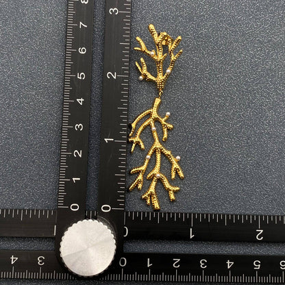 one gold pearl encrusted coral shaped earrings next to a ruler on a grey surface