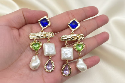 Hand holding multi-stone pearl drop earrings in blue tones with baroque pearls and colored stones