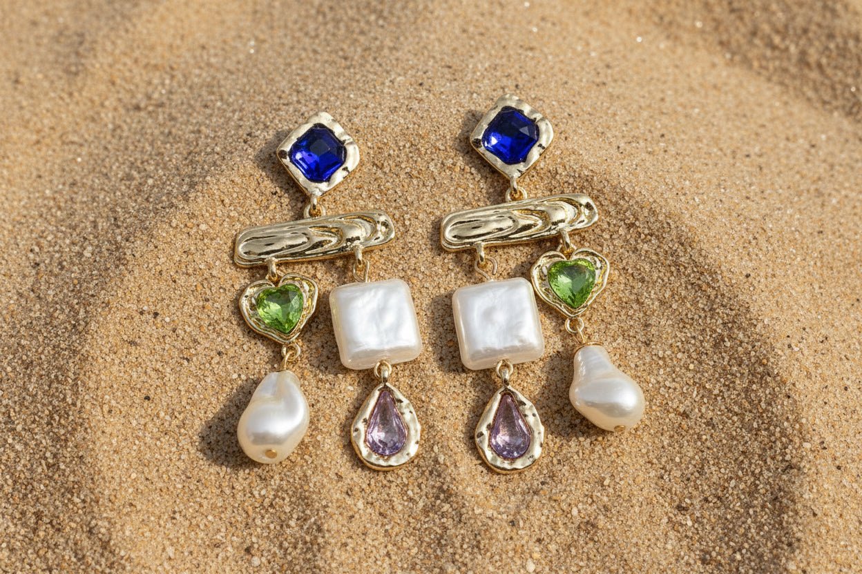Pair of gold earrings with gemstones and pearls on a sandy background