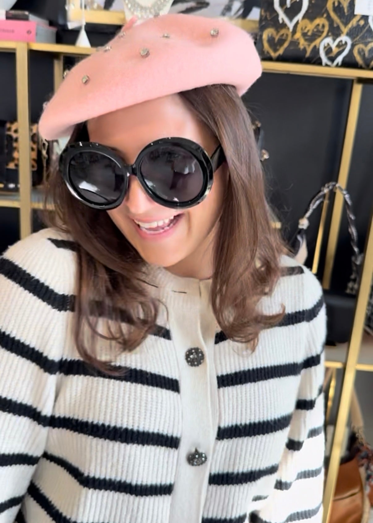 Person wearing a pink beret and black sunglasses with a striped sweater in an indoor setting.