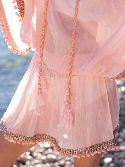 close up of woman wearing a pink swim coverup with tassel trim in an outdoor setting