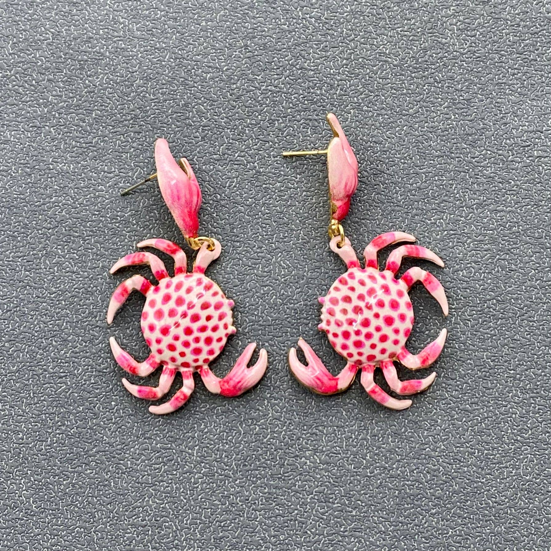 a pair of pink and white crab dangle earrings on grey background