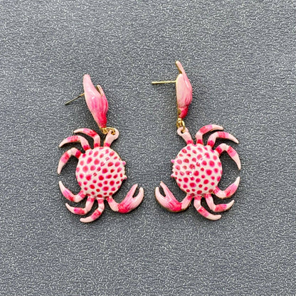 a pair of pink and white crab dangle earrings on grey background