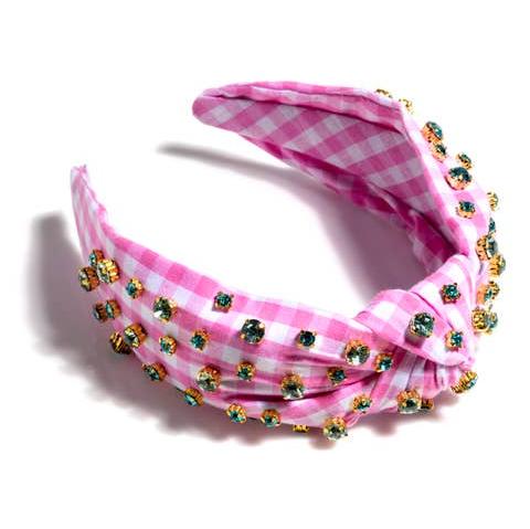 A pink gingham headband with multicolored rhinestone details laying on a white background