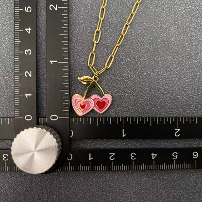 up close view of a pink and red cherry themed pendant necklace with gold chain next to a black ruler laying on a grey background
