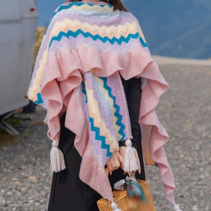 A person wearing a pink and multi-color wrap with tassel trim in an outdoor setting