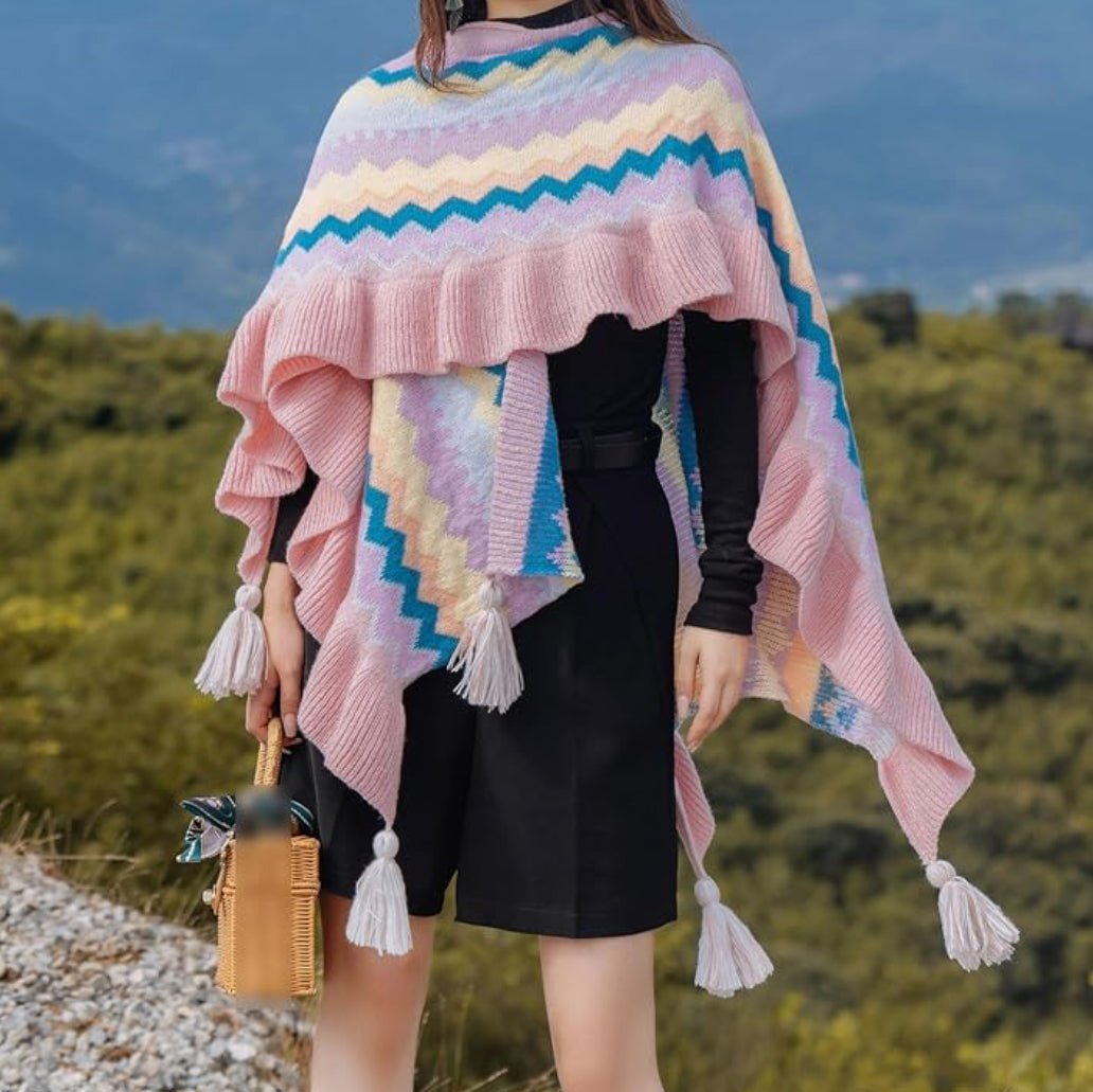 A woman wearing a pink and multi-color shawl wrap with tassel trim in an outdoor setting