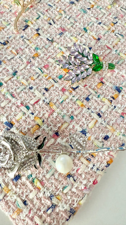 Detail view of nature-inspired jeweled brooches including lavender, rose stem with pearl, on pink tweed fabric