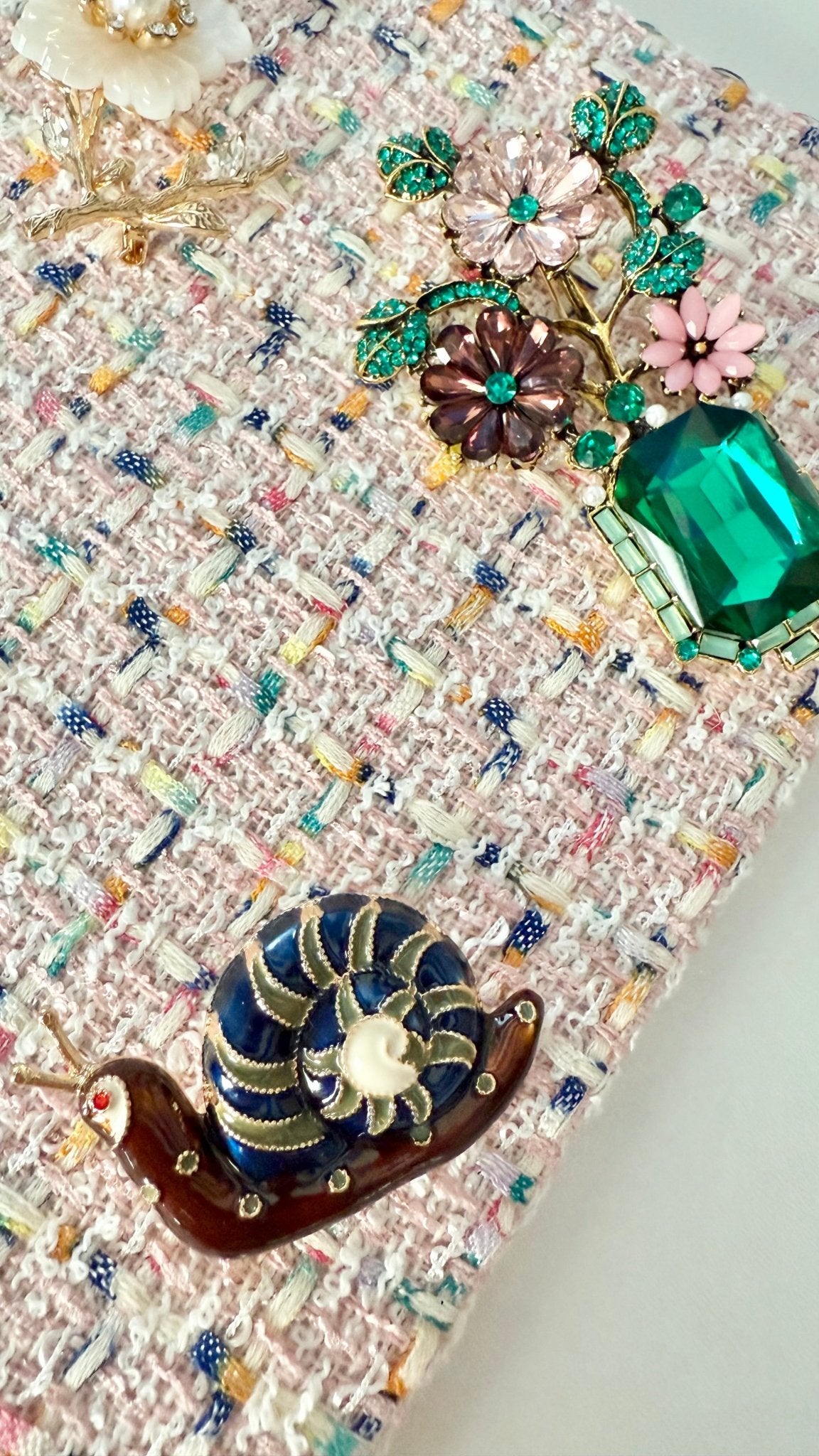 Close-up of crystal and enamel floral brooches pinned on pale pink tweed fabric with rainbow threading
