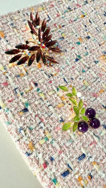 Detail view of nature-inspired jeweled brooches including butterfly, olive branch, on pink tweed fabric