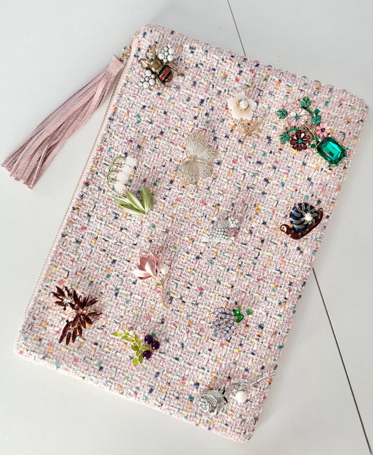 Pale pink tweed clutch pouch with 12 jeweled botanical brooches pinned across the front and pink tassel detail