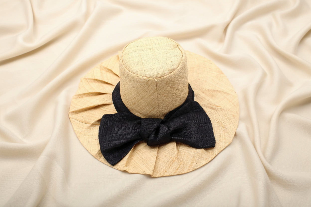 Beige pleated raffia sun hat with a black bow on an ivory background