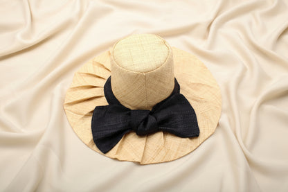 Beige pleated raffia sun hat with a black bow on an ivory background