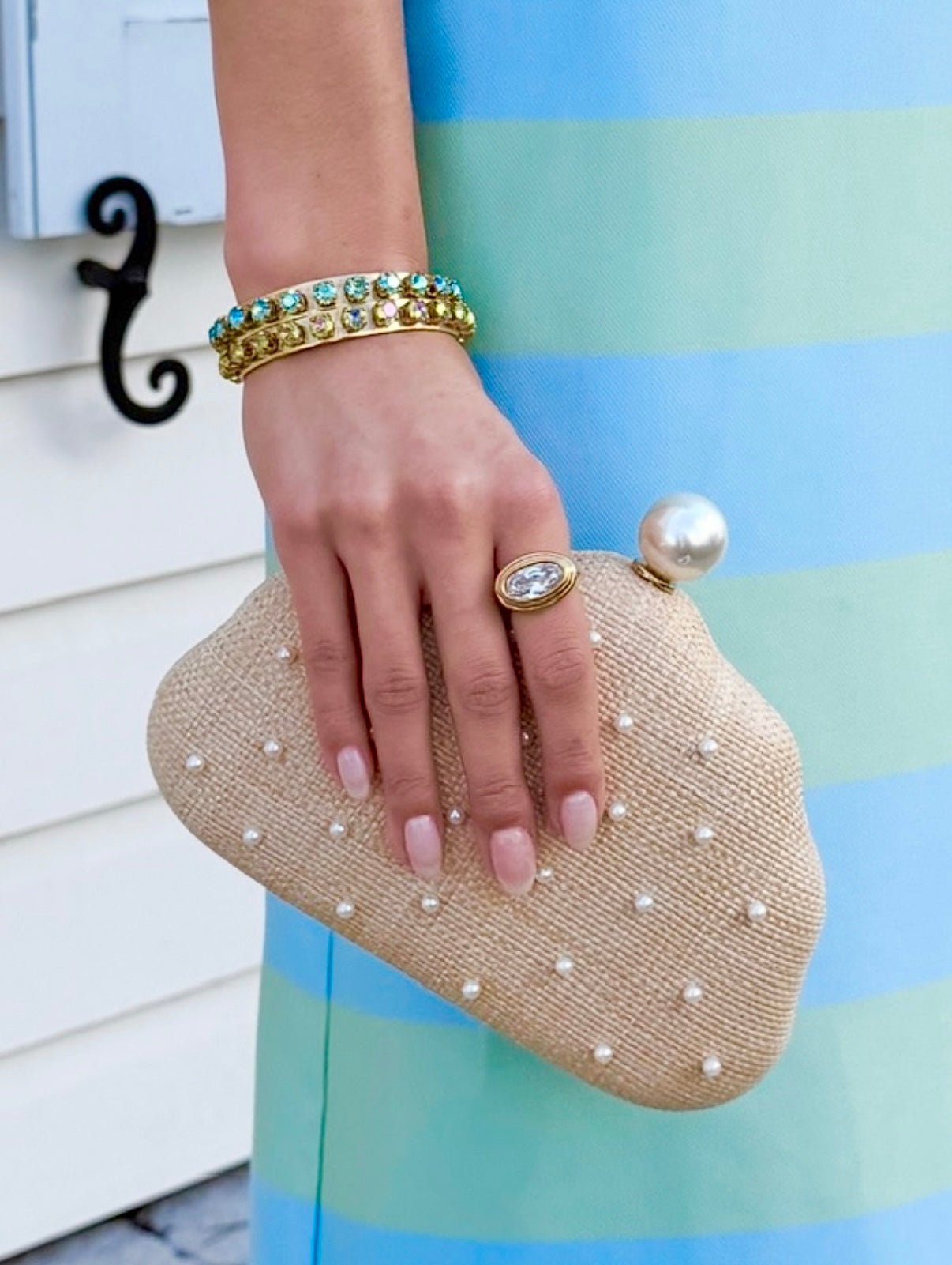 Hand holding a pearl-studded raffia clutch against a striped dress