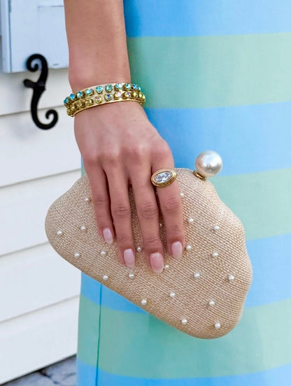 Hand holding a pearl-studded raffia clutch against a striped dress