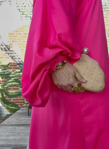 Pearl and raffia clutch purse styled with fuchsia outfit — lifestyle view showing bold color contrast with natural raffia and pearls