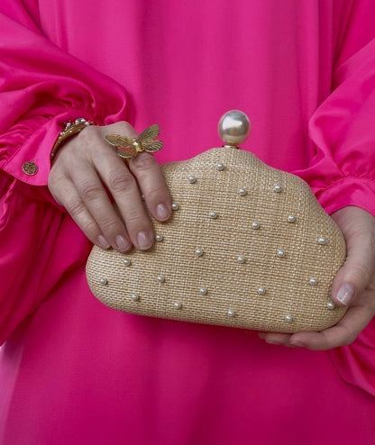 raffia and pearl beaded clutch held by a hand against a pink dress