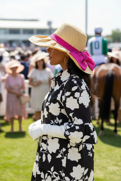 Woman in a floral dress and sun hat with pink ribbon at a horse racing event