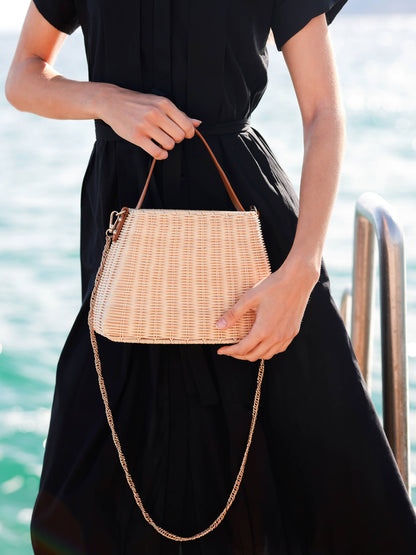 Woman in a black dress holding a rattan handbag by the water