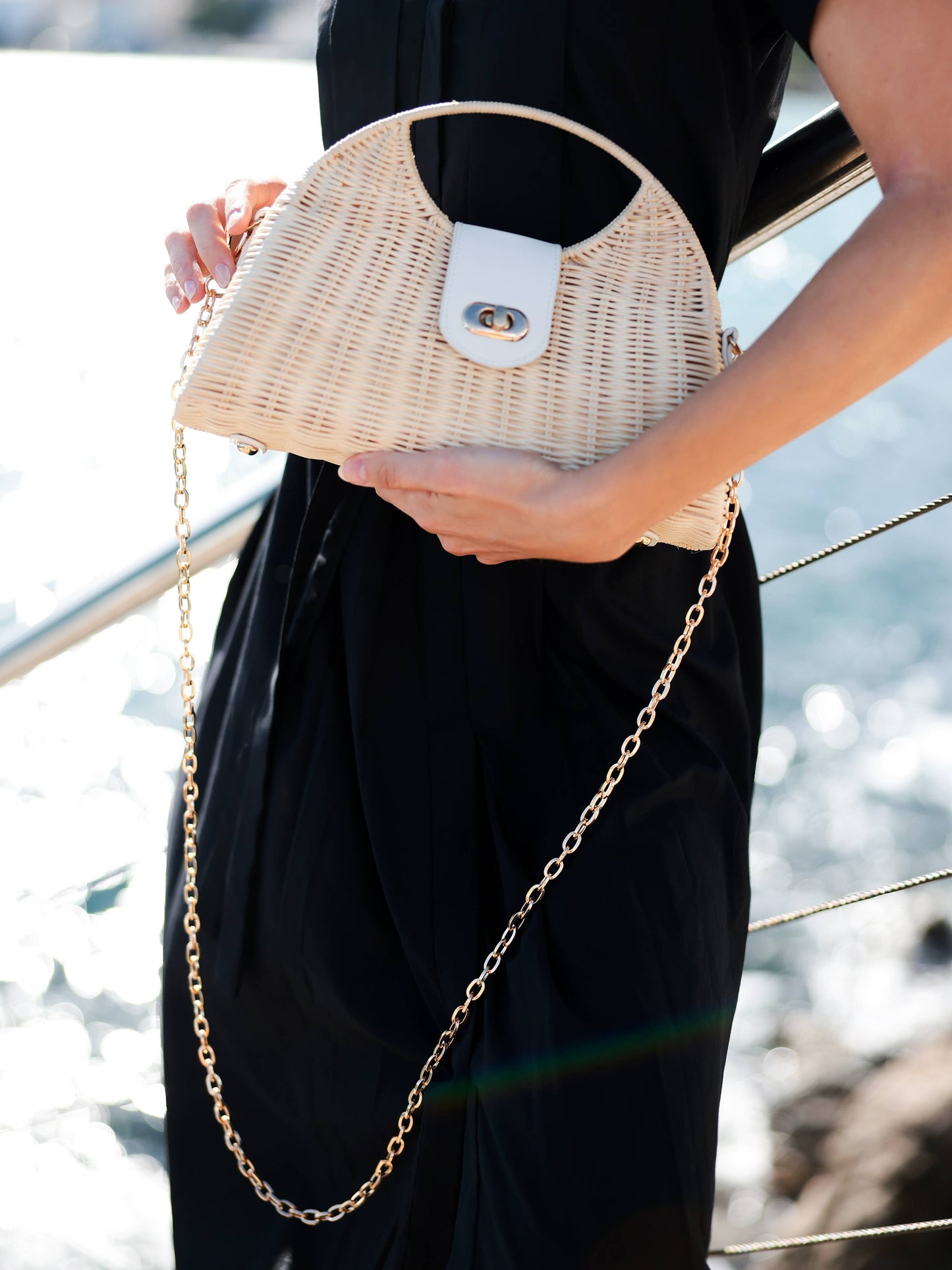 woman in a black dress holding a rattan bag with gold chain in outdoor setting