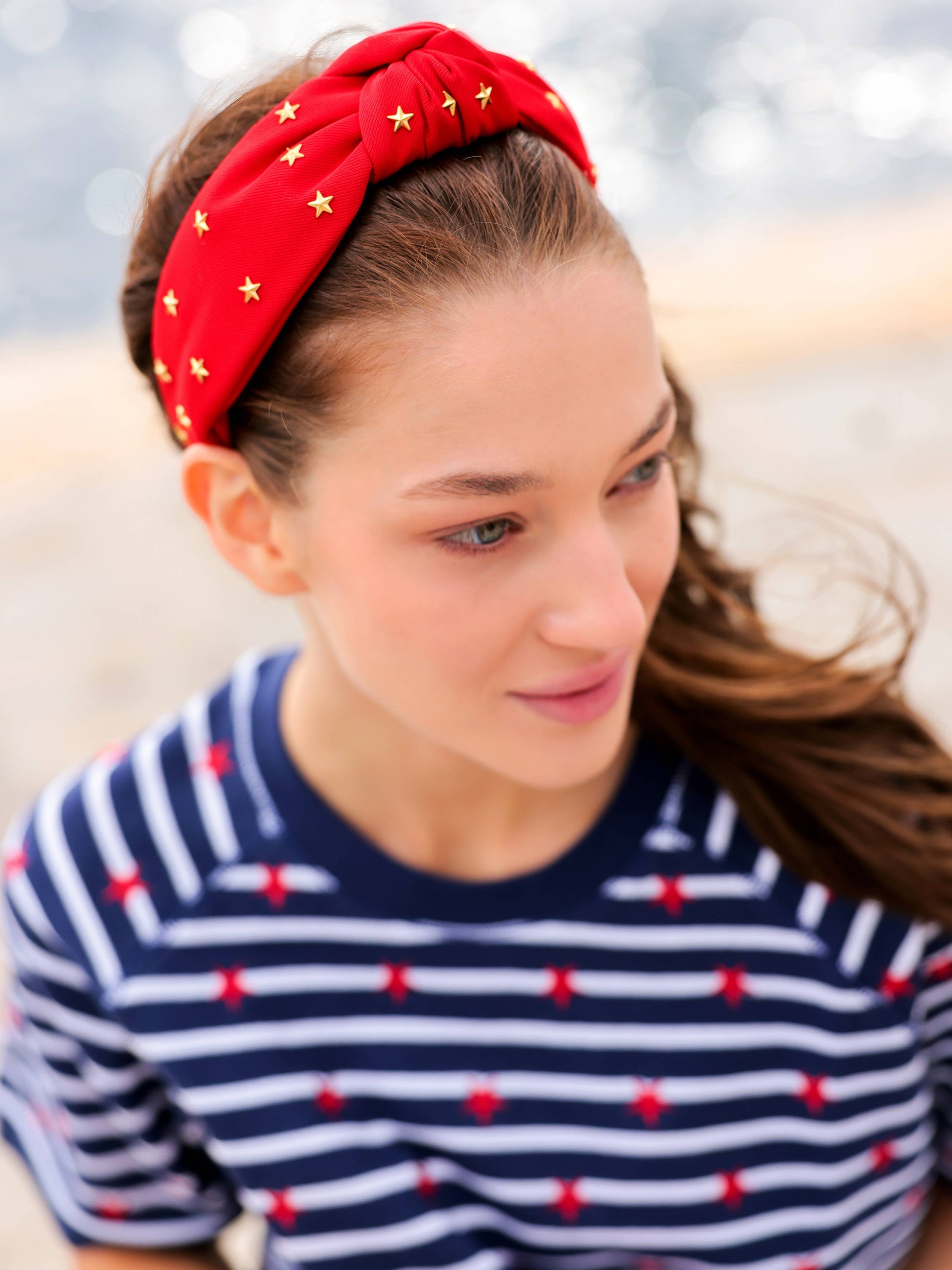 Woman wearing a red headband with gold stars and a striped shirt with red polka dots in a blurred outdoor setting