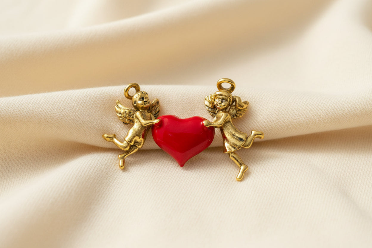 Gold cherubs brooch holding a red heart on a gray background
