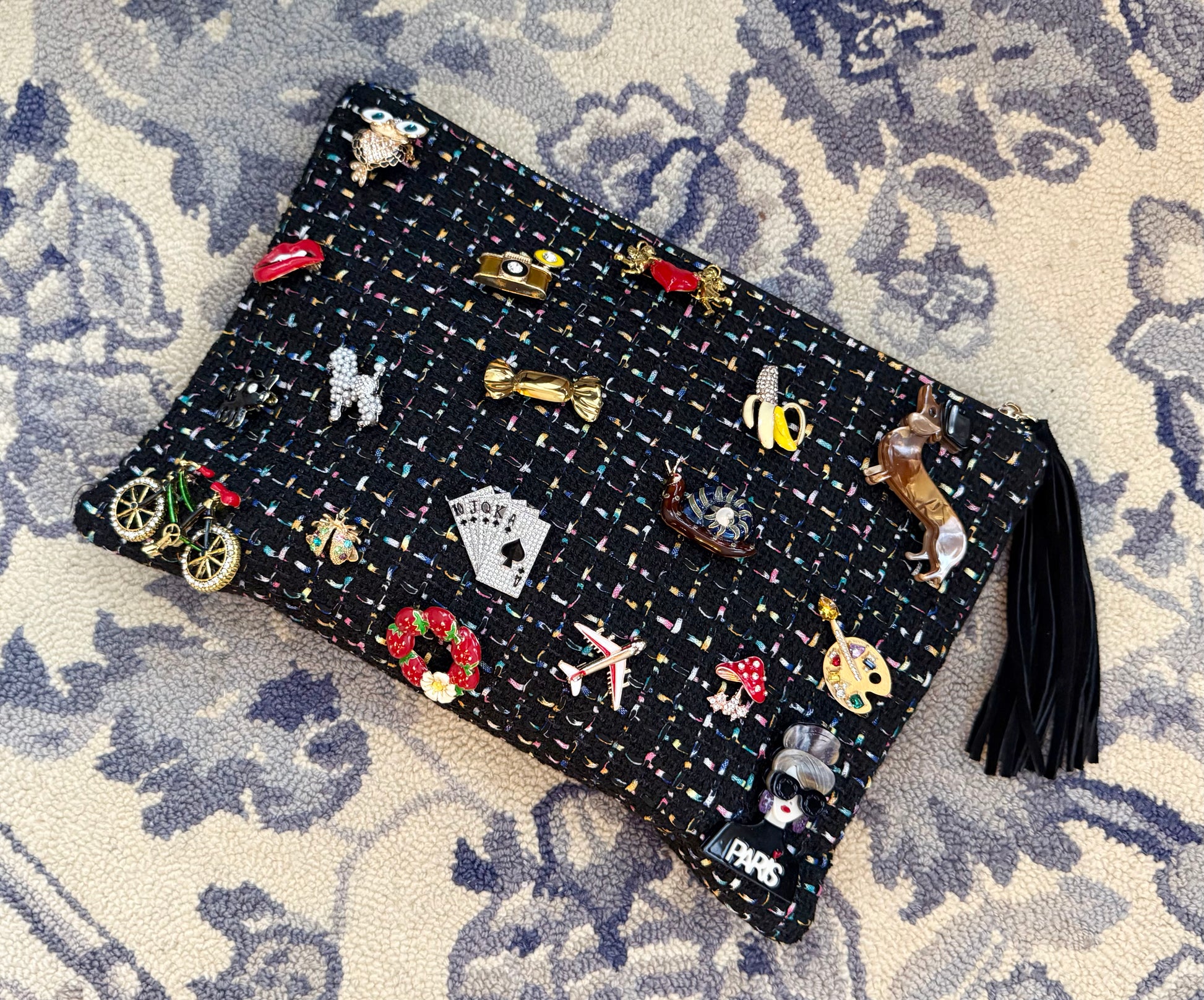 Black clutch bag with tassel with colorful brooches on a patterned surface