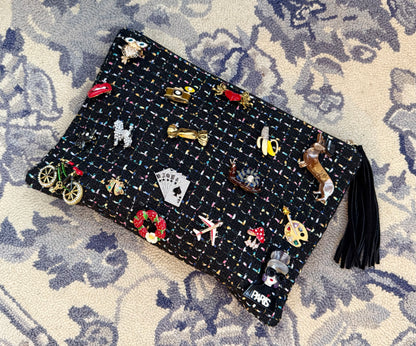 Black clutch bag with tassel with colorful brooches on a patterned surface