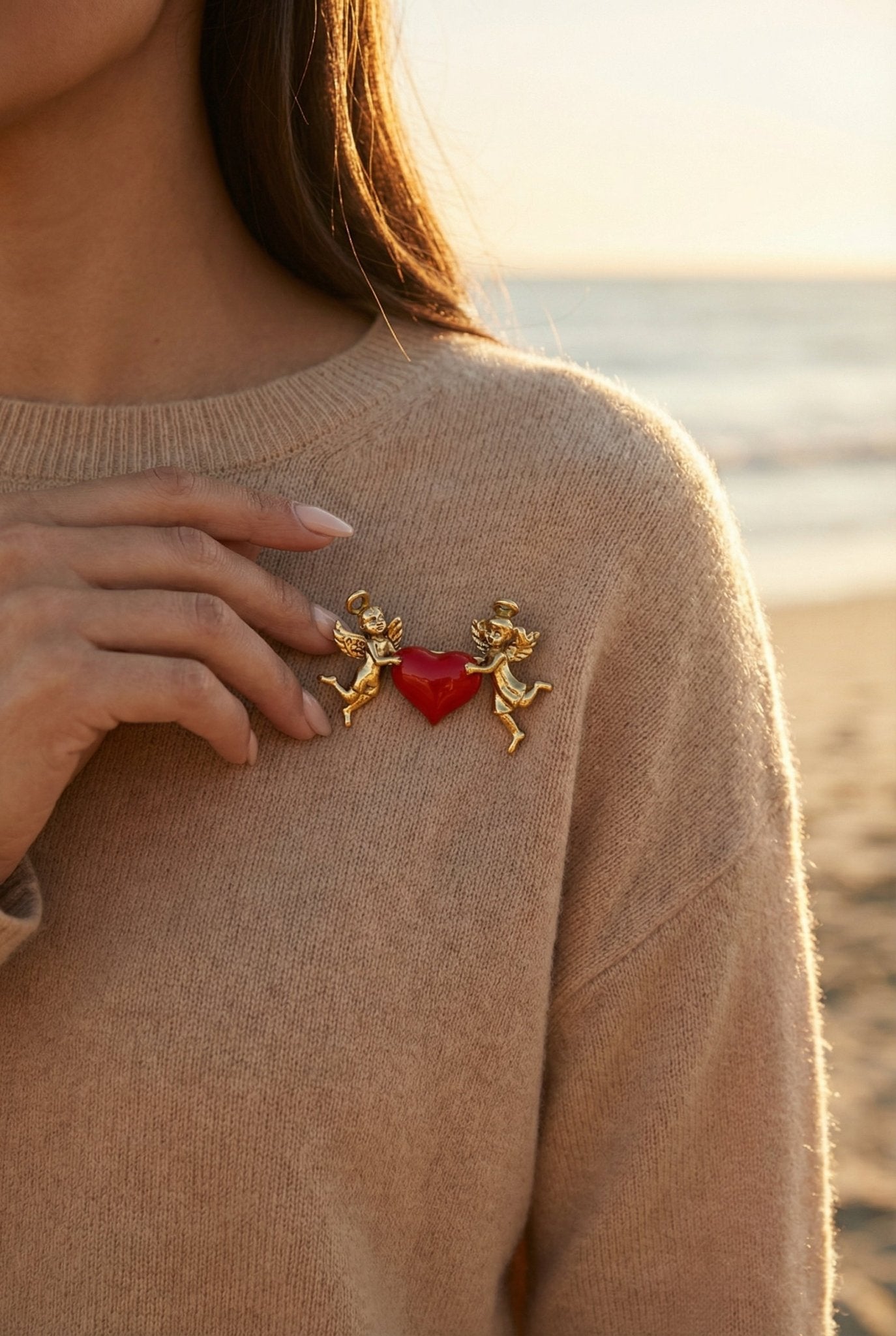 Woman wearing a brooch with cherubs and a red heart on a beige sweater by the sea.