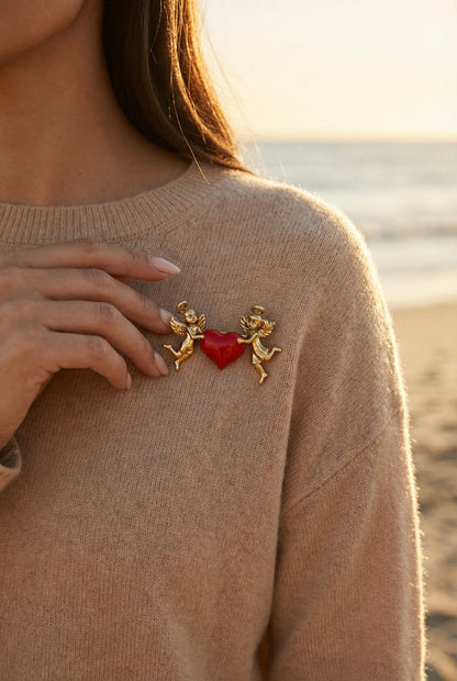 Woman wearing a brooch with cherubs and a red heart on a beige sweater by the sea.