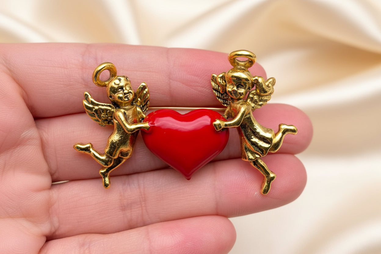Gold cherubs brooch holding a red heart on a hand against a grey background