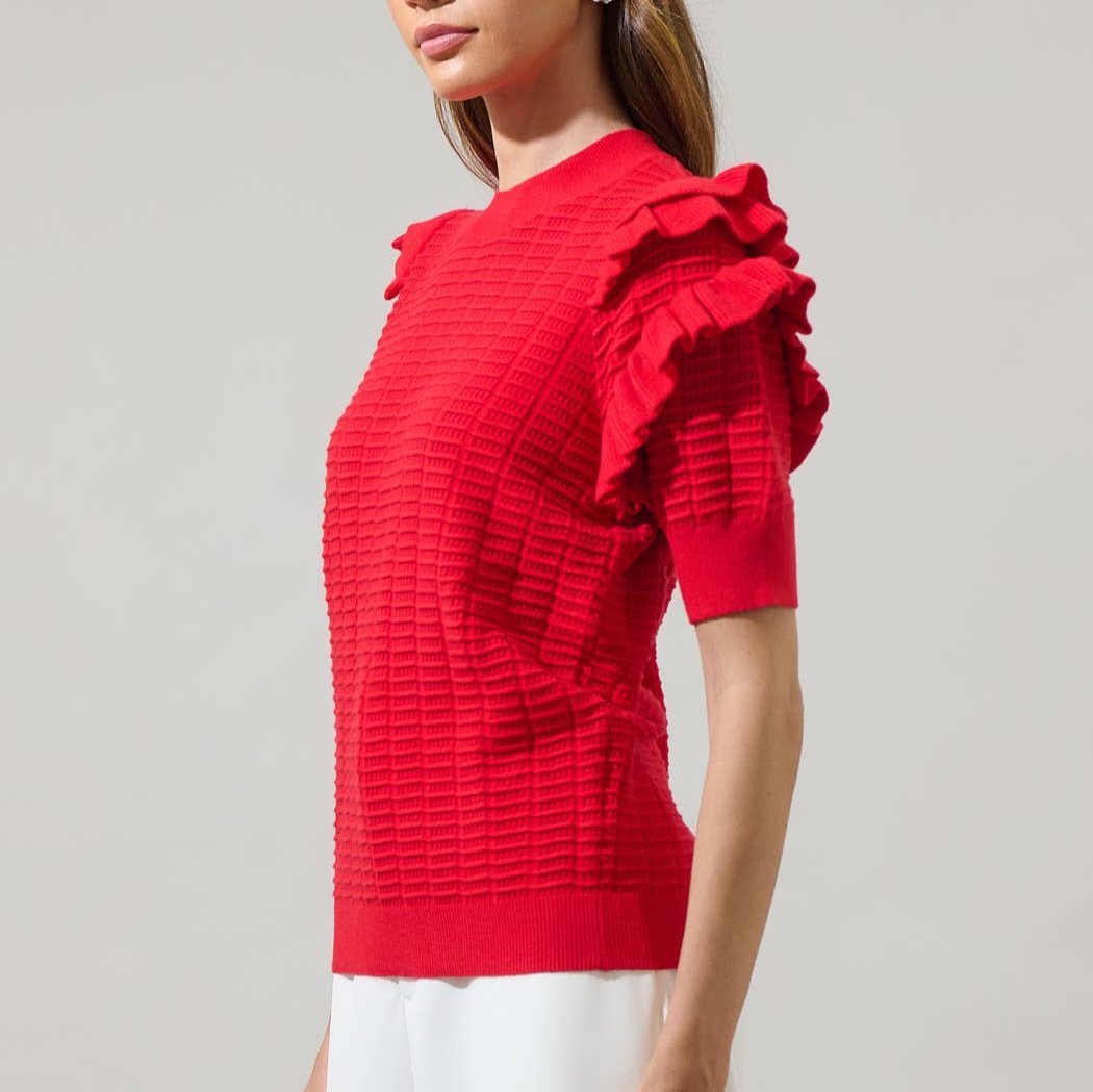 Angled view of a woman wearing a red textured top with ruffled sleeves on a plain background
