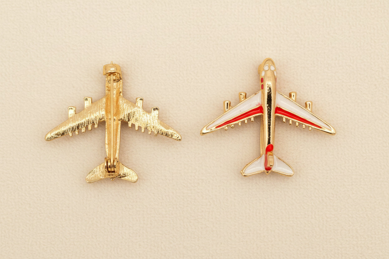 Two airplane-shaped brooches on a textured gray background