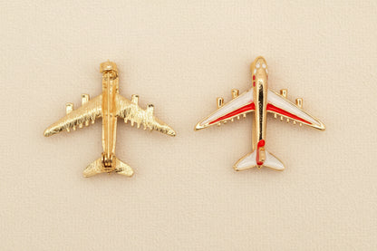 Two airplane-shaped brooches on a textured gray background