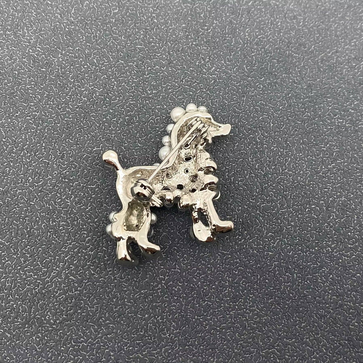 Back view of dog-shaped brooch in a silver color on a textured gray background