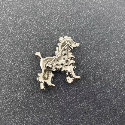 Back view of dog-shaped brooch in a silver color on a textured gray background