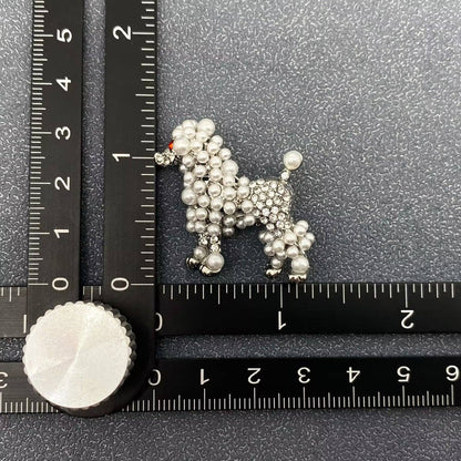 Silver poodle-shaped brooch with pearl and rhinestone embellishment on a textured black surface with a ruler for scale.