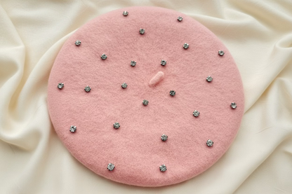 close-up of rhinestone stud detail on light pink beret on an ivory fabric surface