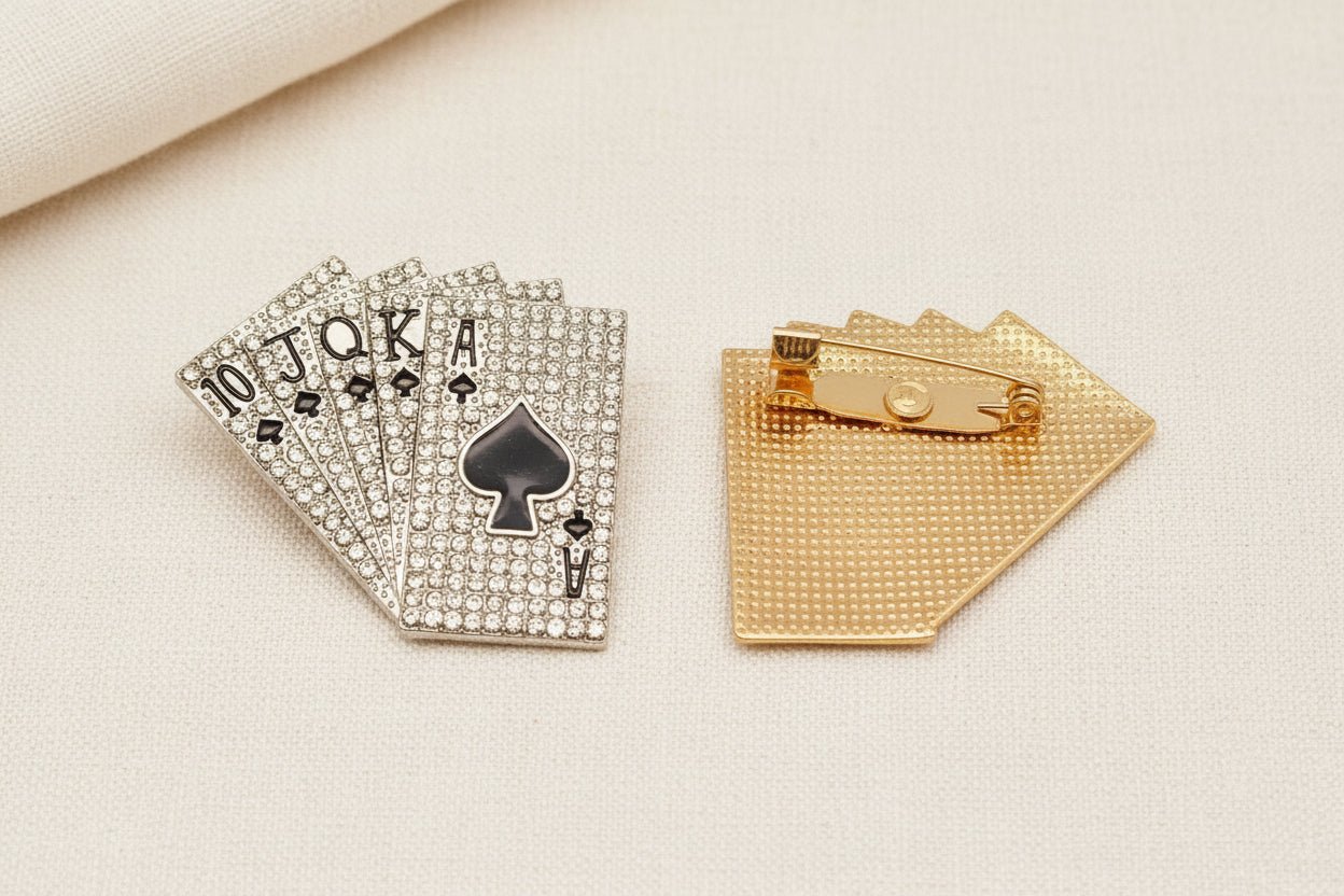 two royal flush playing cards brooches with one front side up to show the crystals and the other showing the back view and pin closure against an ivory fabric background
