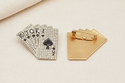 two royal flush playing cards brooches with one front side up to show the crystals and the other showing the back view and pin closure against an ivory fabric background