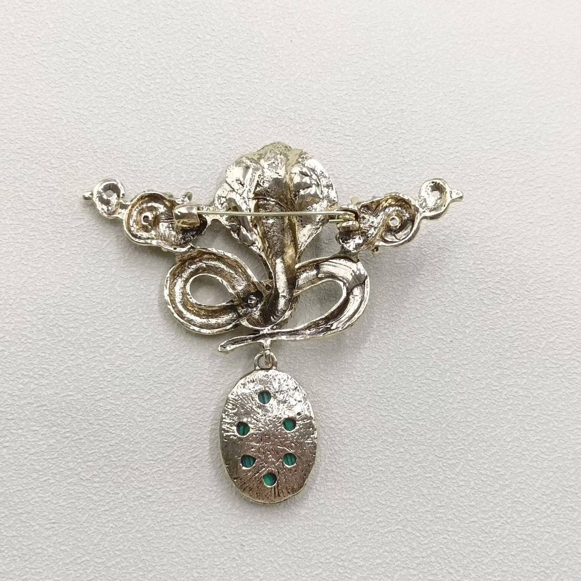 back view of serpent brooch with silver color on a light gray background