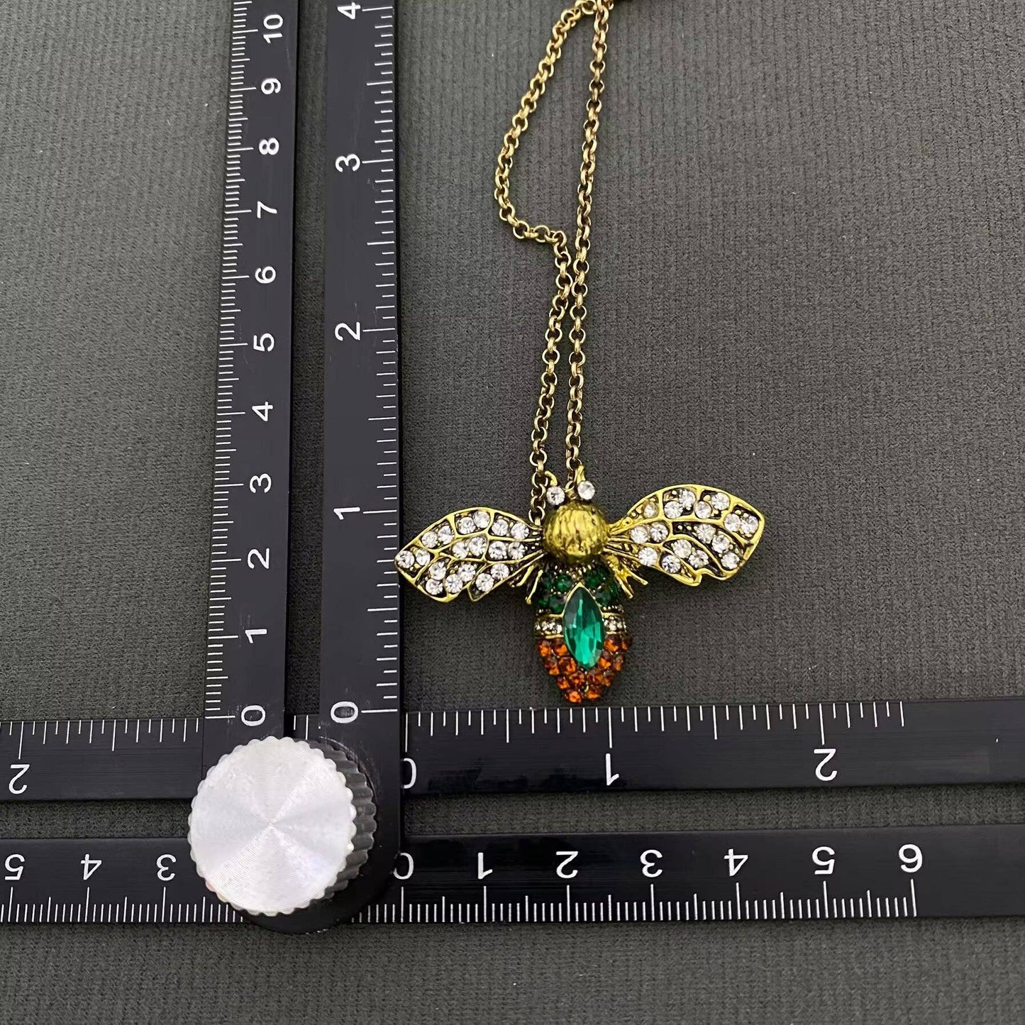 up close view of a bee brooch next to a ruler on a black background