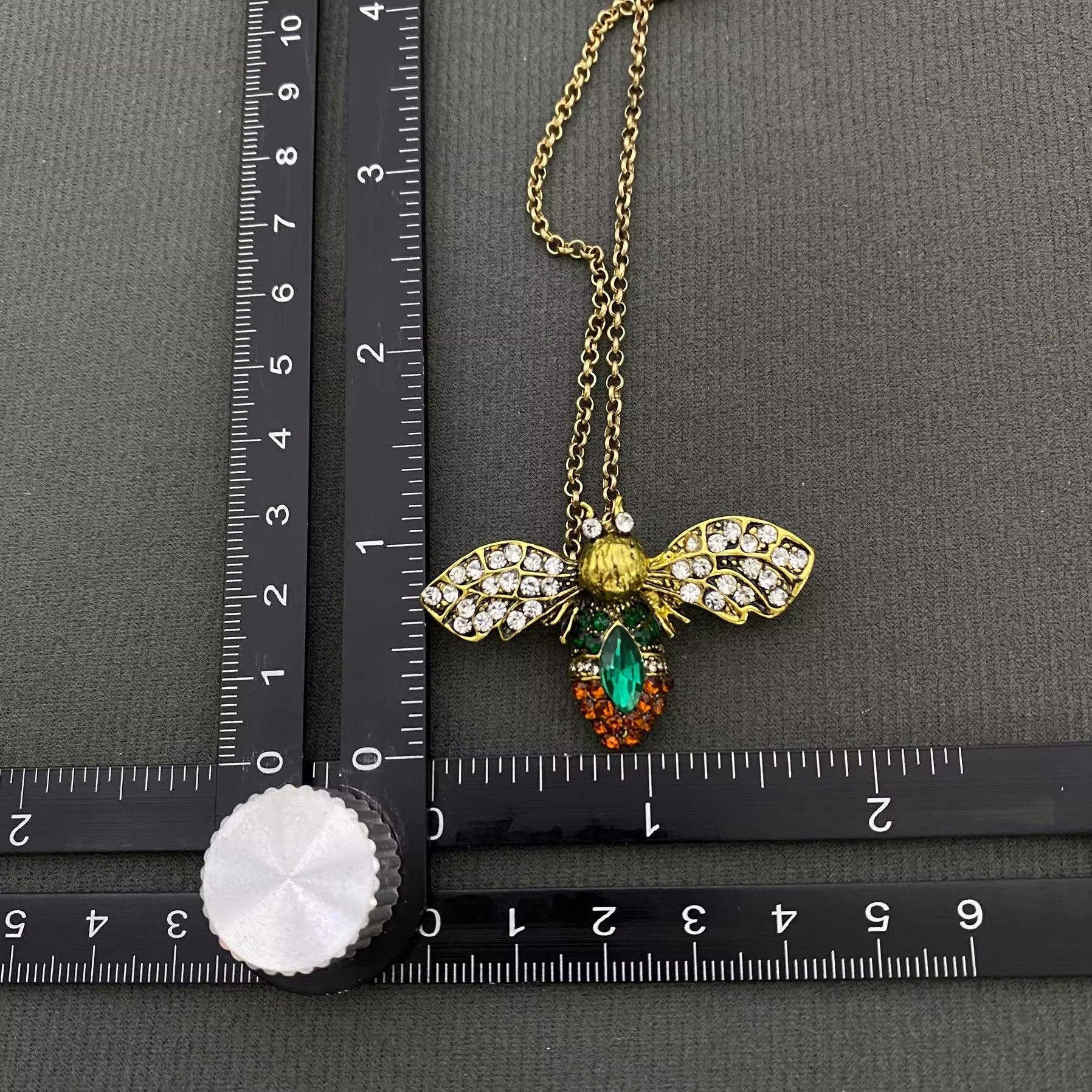 up close view of a bee brooch next to a ruler on a black background